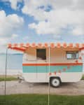 Vintage caravan with orange and white striped awning by a lakeside, decorated with bunting.