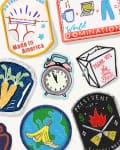 Colorful embroidered merit badges with humorous themes like "World Domination," "Jet-Lagged," and "Made in America."