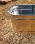 Galvanized metal tub on dry grass in a backyard setting.