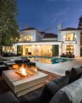 Modern luxury home exterior with pool, patio seating, fire pit, and large windows at dusk.
