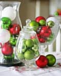 Glass jars filled with red, green, and white Christmas ornaments on a table.