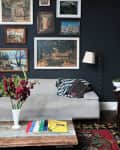 Living room with gray sofa, gallery wall of paintings, wooden coffee table, red flowers in vase, and colorful magazines.