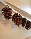 Pinecone garland hanging on a white mantel in a softly lit room.