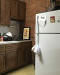 Small kitchen with wooden cabinets, white appliances, utensils in a holder, and a framed picture on the counter.