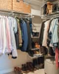 Organized walk-in closet with hanging clothes, shoes, and woven storage baskets on shelves.