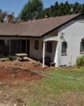 Single-story house with a sloped roof, sliding glass doors, and a small patio in a backyard with sparse grass and plants.