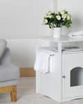 White side table with a cabinet, potted flowers, and a towel, next to a gray sofa and a green plant.