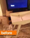 Small white table with angled legs on plastic sheet in living room, TV and decor on wooden console behind.