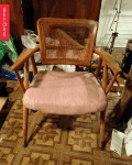 Worn wooden chair with a damaged cane backrest and faded pink cushion on patterned floor.