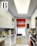 Narrow kitchen with stainless steel appliances, red blinds, and cluttered countertops.