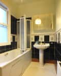 Bathroom with black and white tiles, a bathtub with folding screen, pedestal sink, and mirrored cabinet.