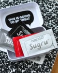 Sugru packets in a white container on a black and white notebook with a pen.