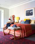 Bedroom with stone fireplace, red patterned rug, orange bedspread, yellow lamps, and wooden side tables.