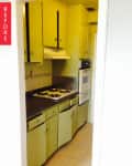 Narrow kitchen with green cabinets, gas stove, and double oven.