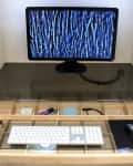 Computer monitor with abstract screen, keyboard, and mouse on a pull-out desk with storage compartments.