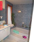 Bathroom with blue tiled walls, white vanity, bathtub, and clothes on the floor.