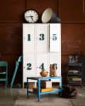 White numbered lockers with a clock, teal chair, blue cart, and decor items in an industrial-style room.