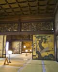 Traditional Japanese room with tatami mats, ornate gold wall panels, and soft lighting from floor lamps.