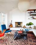 Mid-century modern living room with red and blue chairs, geometric rug, white sofa, and a fireplace.