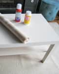 White coffee table with a roll of contact paper, spray adhesive, and Mod Podge bottle on top.