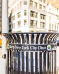 Trash can with "Keep New York City Clean" sign, yellow taxi, and blurred city buildings in the background.