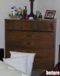 Wooden dresser with various toiletries, a lamp, and a framed photo on top, pillows on the floor in front.