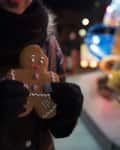Person holding a gingerbread cookie at a festive night market with colorful lights in the background.