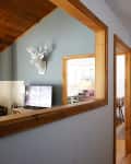 Hallway view into living room with mounted deer head, TV, and kitchen glimpse through wooden-framed openings.
