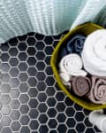 Basket of rolled towels on black hexagonal tile floor next to a textured shower curtain.