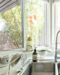 Kitchen sink with a modern faucet, soap dispenser, and window view of bamboo plants.