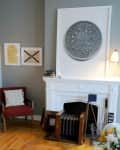 Living room with a white fireplace, large coin art, red chair, and framed wall art.