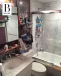 Cluttered bathroom with marble countertop, shower with glass doors, and various toiletries on shelves and sink.