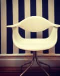 White modern chair with curved arms in front of a navy and white striped wall.