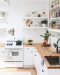 Bright kitchen with white cabinets, wooden countertops, open shelves, potted plants, and a mint green fridge.