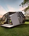 Modern geometric tiny house with large windows on a grassy field at sunset.