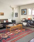 Living room with black leather sofa, colorful cushions, tribal rug, glass coffee table, and wall art, featuring a skull decor.
