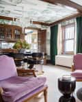 Living room with purple armchairs, a round glass coffee table, brick fireplace, and green curtains.