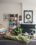 Living room with a white Christmas tree, black fireplace, bookshelves, and a wicker chair with a blue and white pillow.