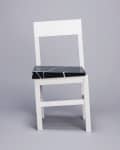 White chair with a black marble seat on a gray background.