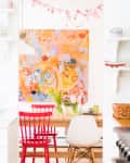 Dining area with red chairs, abstract orange artwork, and a wooden table with flowers in vases.
