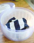 Plastic salad spinner with a striped sock inside, on a wooden countertop.