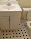 Small bathroom with white vanity, chrome faucet, and toilet on black and white tiled floor.
