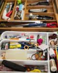 Kitchen drawer with organized utensils and a cluttered tray of miscellaneous items like pens, scissors, and chargers.
