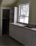 Dimly lit kitchen with white cabinets, a sink, and a window. Doorway leads to another room. Red "Before" label on the left.