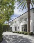 Two-story white house with large windows, palm trees, and a circular driveway.