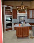 Spacious kitchen with wooden cabinets, island, chandelier, and double oven.
