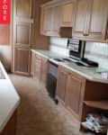 Narrow kitchen with wood cabinets, white countertops, and a black stove.