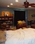 Bedroom with a wooden bed, ceiling fan, TV on wall, bookshelf, and view into a bathroom.