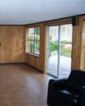 Empty room with wood-paneled walls, tiled floor, sliding glass door, and a black armchair in the corner.