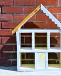 Wooden dollhouse with scalloped roof against a brick wall, labeled "Before" on the left.